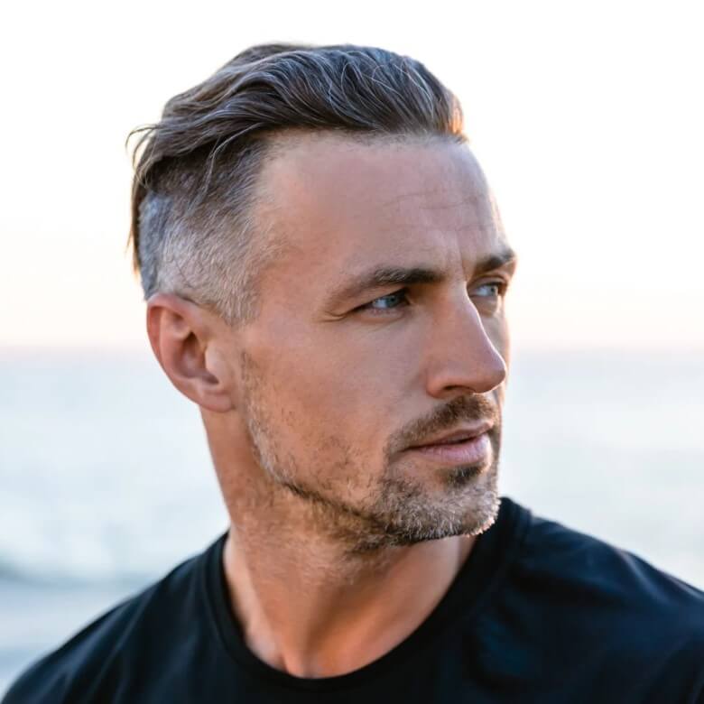 Der Silver Fox Taper betont graues Haar mit klaren Konturen und moderner Struktur. Der 3‑Tage‑Bart sorgt für einen frischen, jugendlichen Kontrast. Ideal für Männer ab 50, die graues Haar stilvoll und modern tragen möchten.